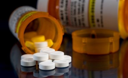 a close up of a tipped over orange container with white pills spilling onto a black surface